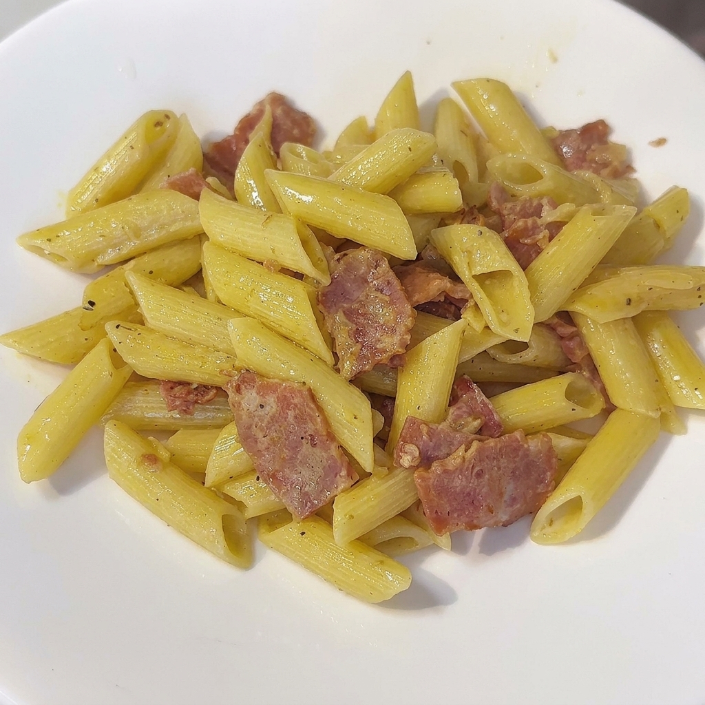 A pan of creamy penne pasta being stirred with a spatula.