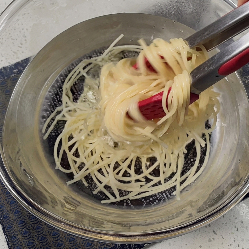 Cooked spaghetti being drained in a metal colander.
