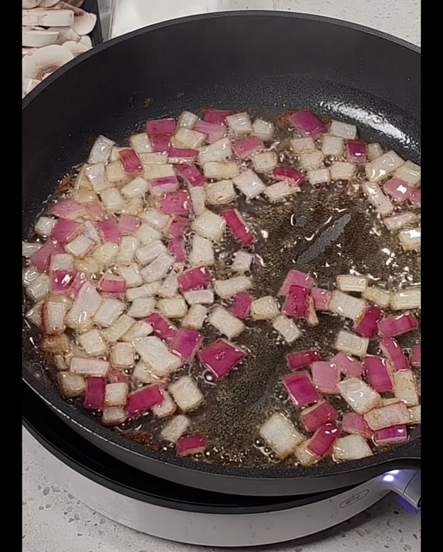 Strips of bacon being added to a pan containing softened, diced red onions.