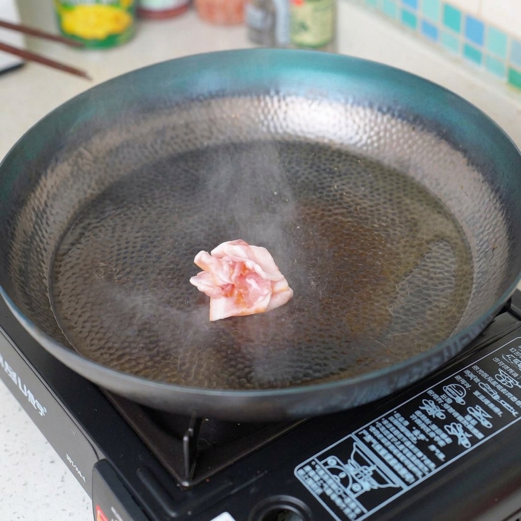 Bacon pieces frying in a hot skillet, becoming crisp.
