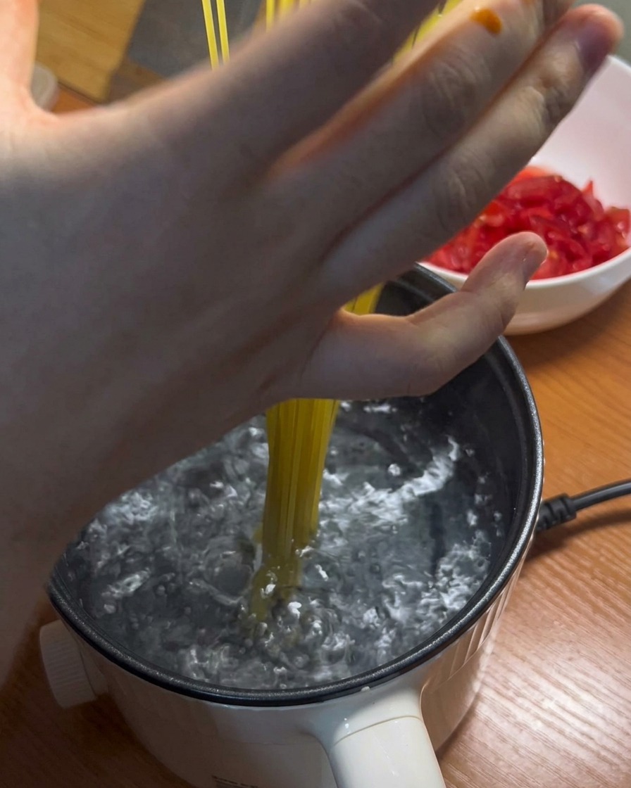Long spaghetti noodles being added to a pot of boiling water.