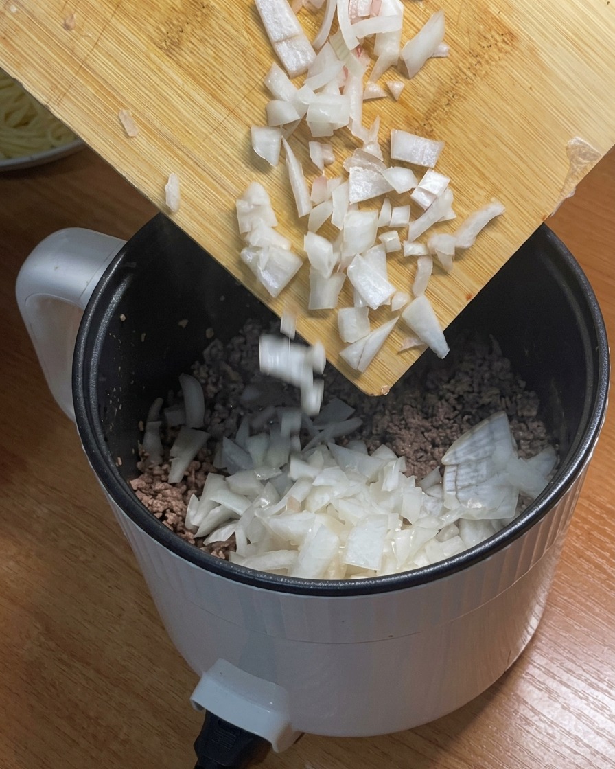 Chopped white onions being added into the pot containing browned minced beef.
