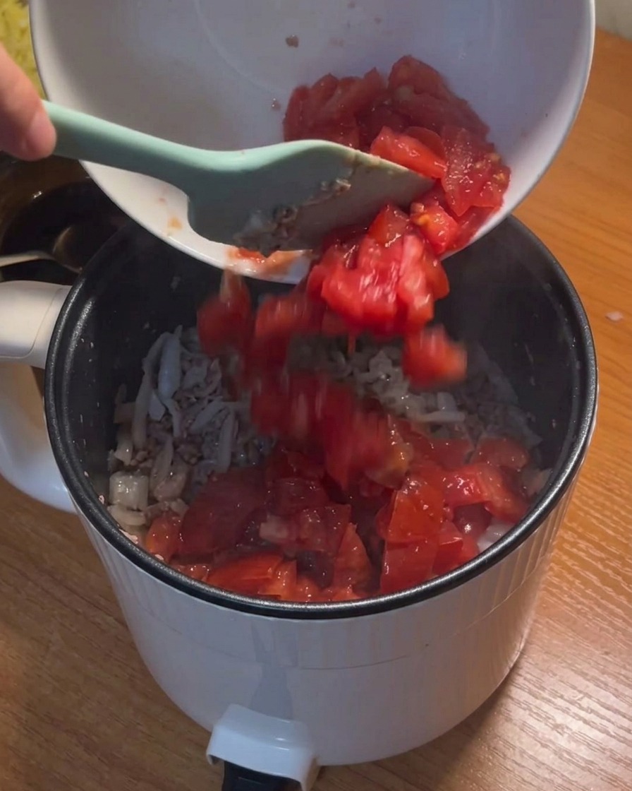 Diced tomatoes being poured from a white bowl into the pot with sautéed beef and onions.