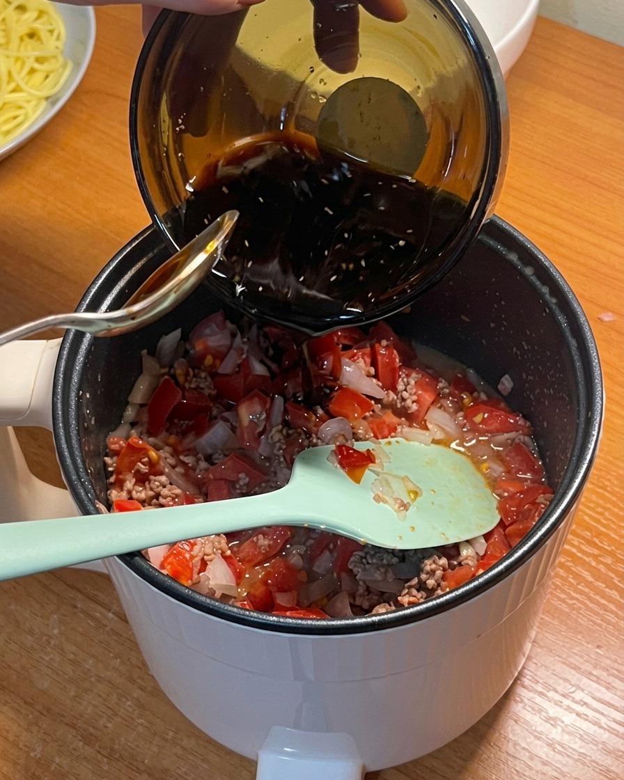 Dark seasoning sauce being poured from a bowl into the pot with tomatoes, beef, and onions.