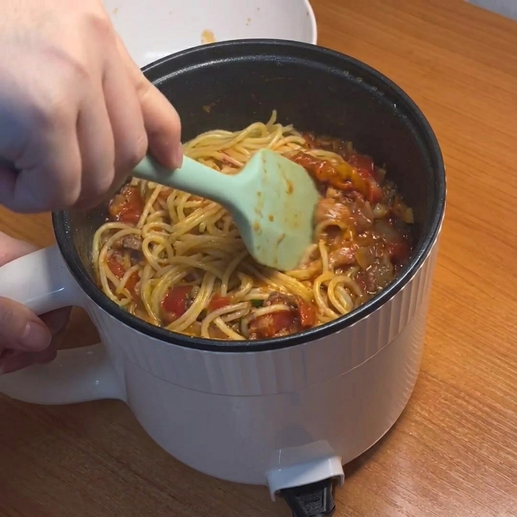 Spaghetti being tossed and coated in the thick red tomato meat sauce.