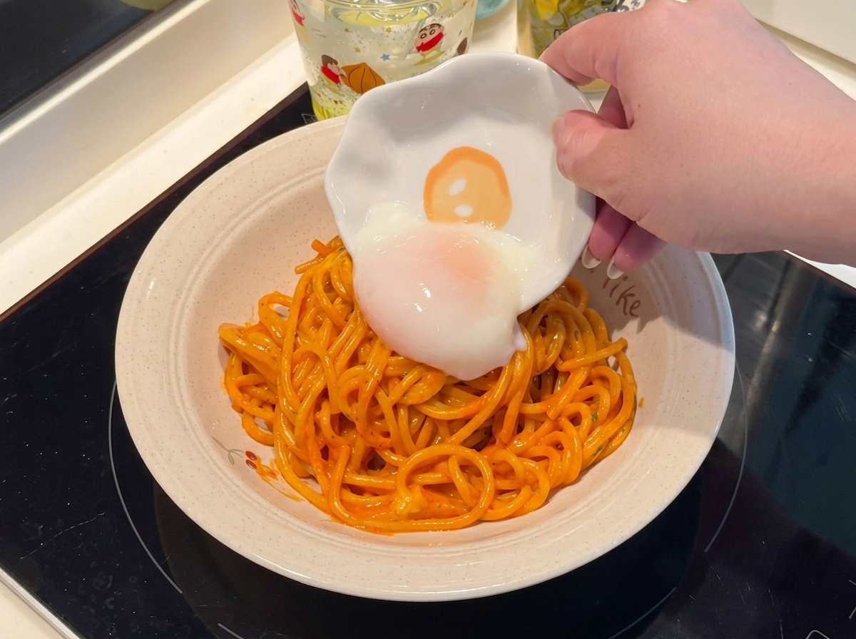 A soft-boiled egg being placed onto a plate of spicy spaghetti.
