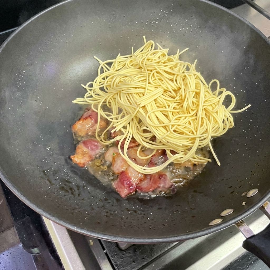 Spaghetti noodles being added to the wok with bacon.