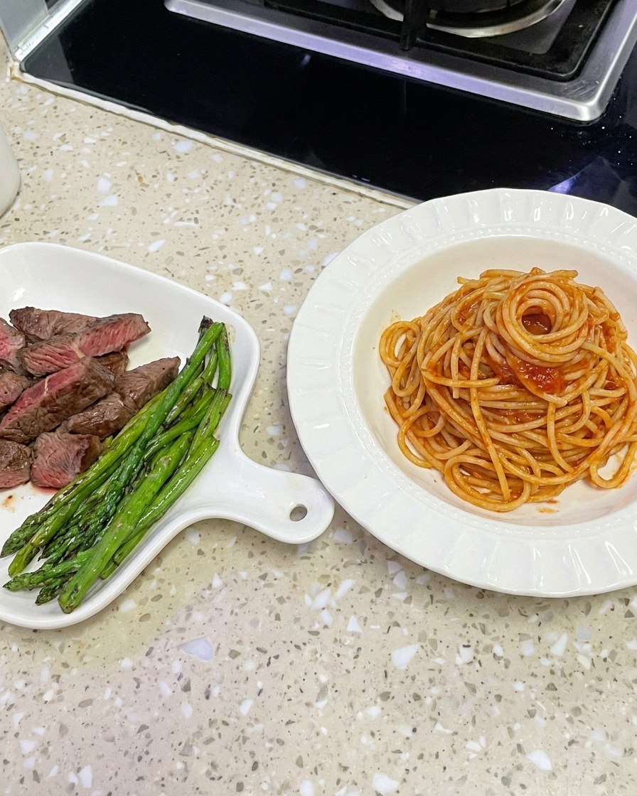 Saucy spaghetti being lifted from a wok with tongs to be plated in a white bowl.