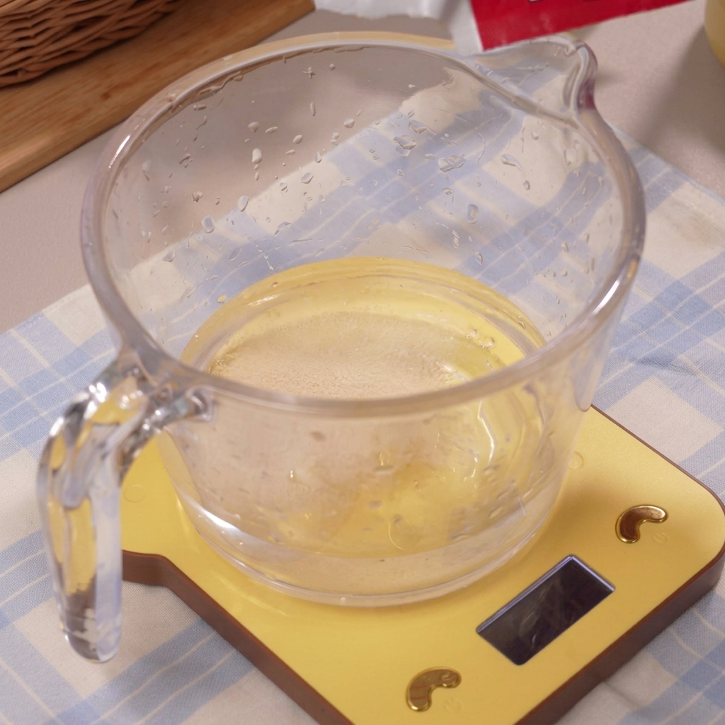 The yeast dissolving into the clear ice water inside the measuring cup.