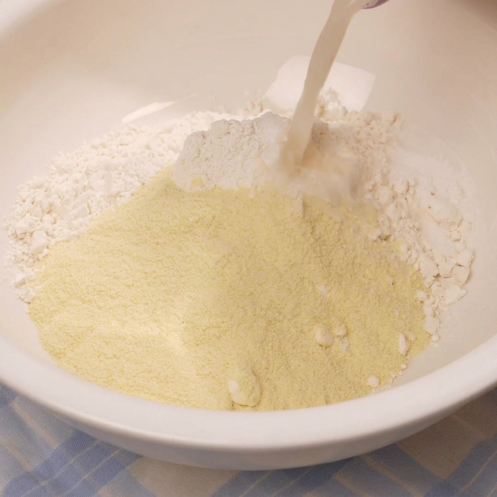 Pouring a milky yeast liquid into a white mixing bowl filled with a mound of flour and dry ingredients.