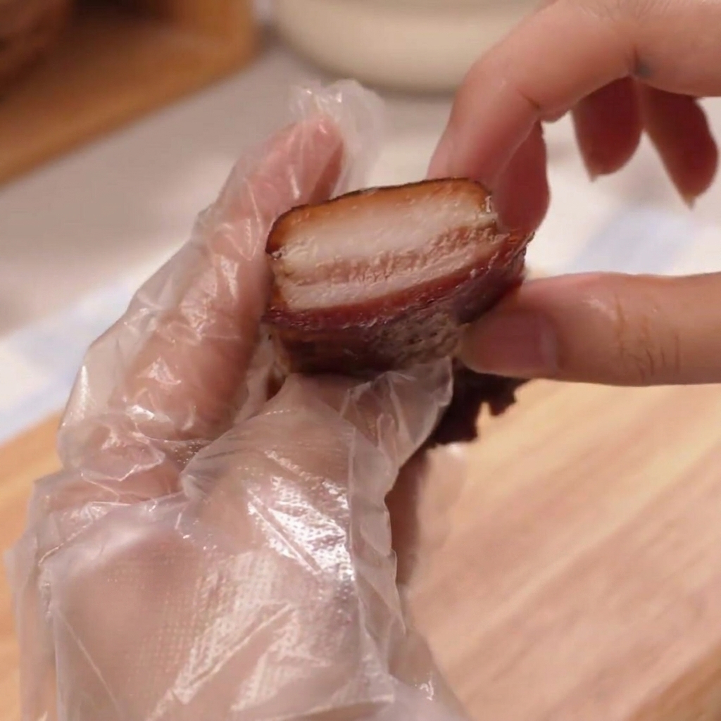 A gloved hand holding up a thick, juicy slice of roasted ham.