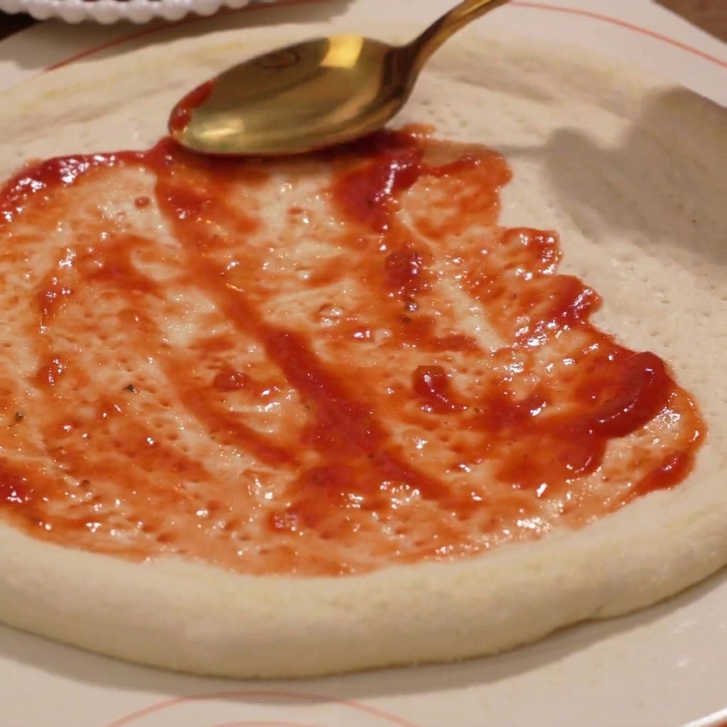 Tomato sauce being spread evenly over the raw pizza dough base.