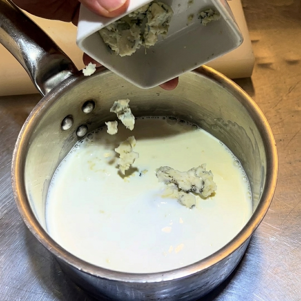 Dropping crumbled blue cheese into a saucepan of milk and cream.