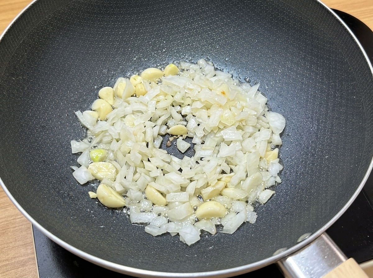 Chopped garlic and diced onions sizzling in cooking oil inside a dark pan.