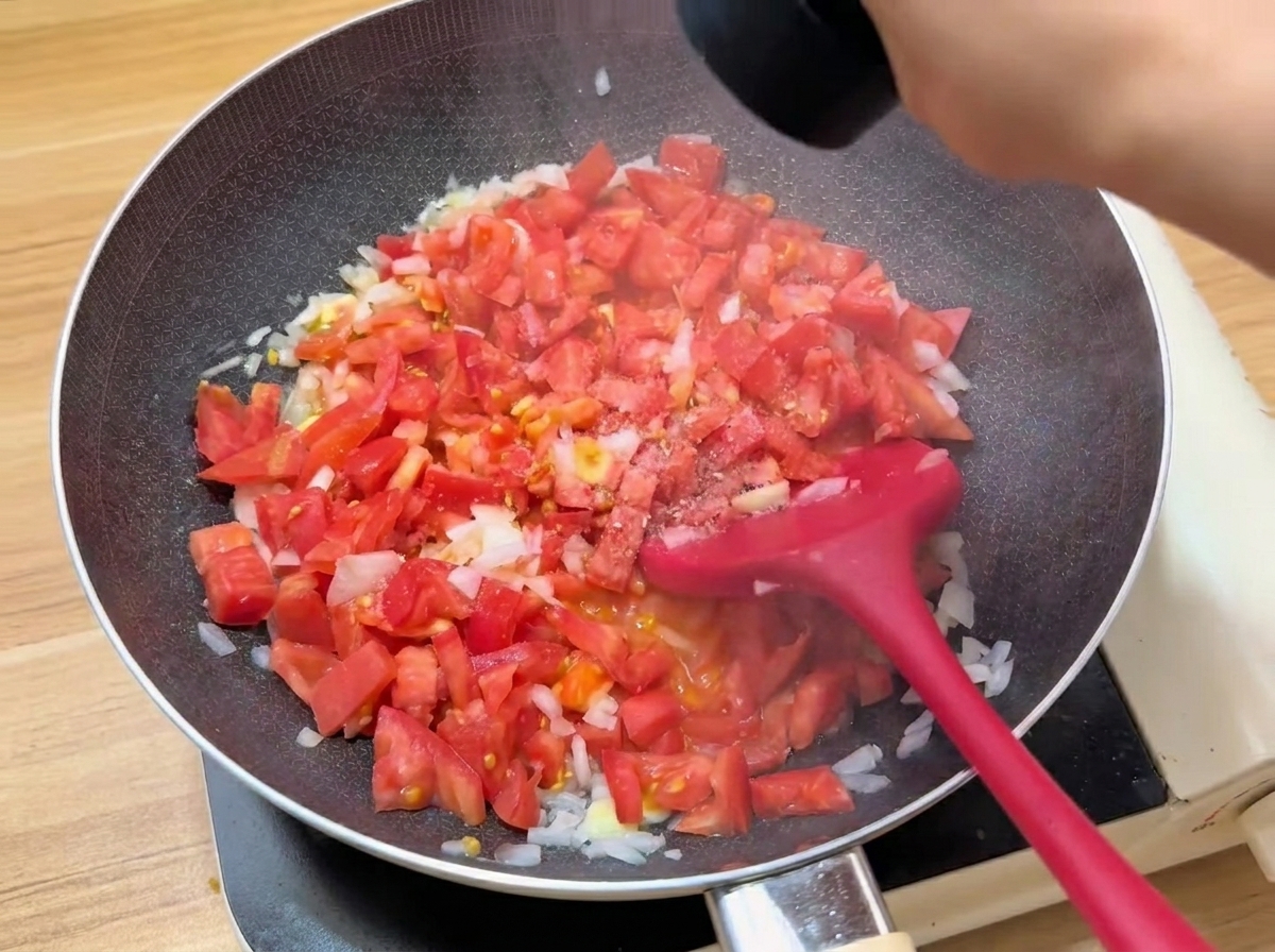 Diced tomatoes cooking in a pan with seasonings being added.