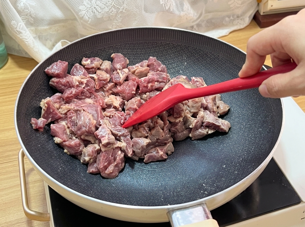 The beef cubes sizzling in the pan, showing a nicely browned surface.