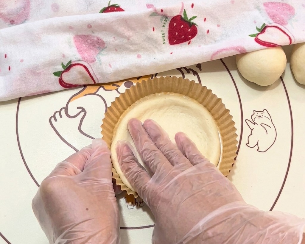 The dough being carefully shaped into the paper tray with gloved hands.