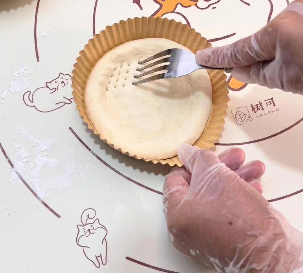The fork creating small indentations across the raw dough base.