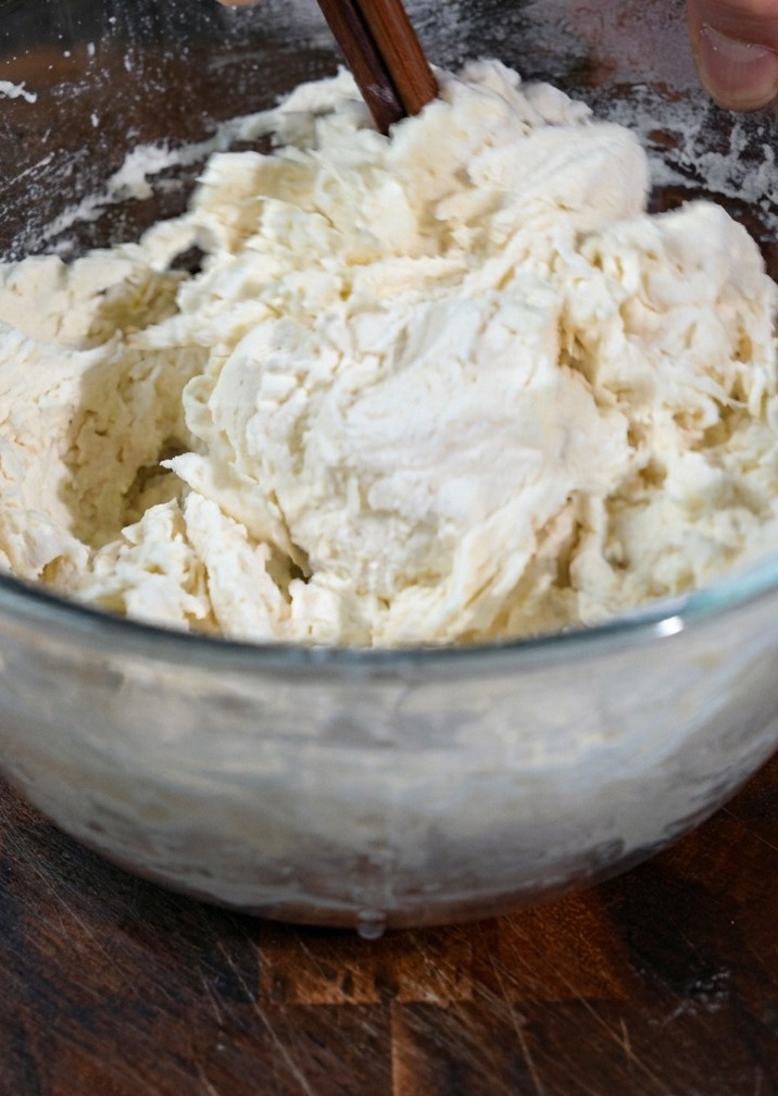 Dough being kneaded by hand on a wooden surface.