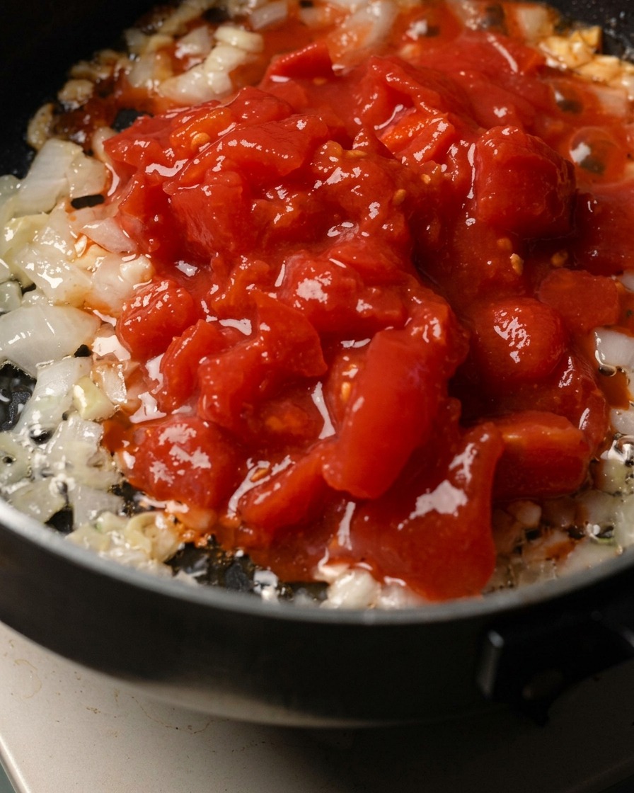 Chopped onion, garlic, and crushed tomatoes cooking in a pan.