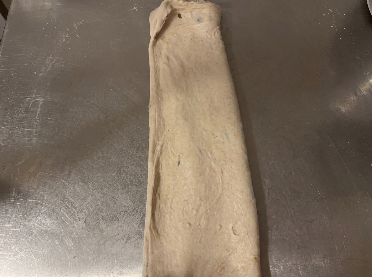 The raw dough folded into a neat, rectangular shape on the stainless steel counter.