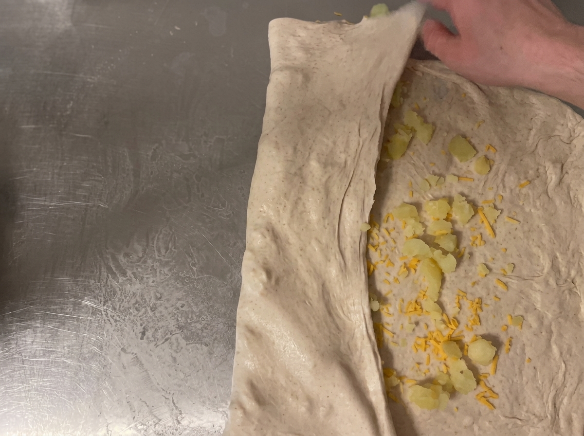 The dough being rolled up on the counter to secure the cheese and potato filling inside.