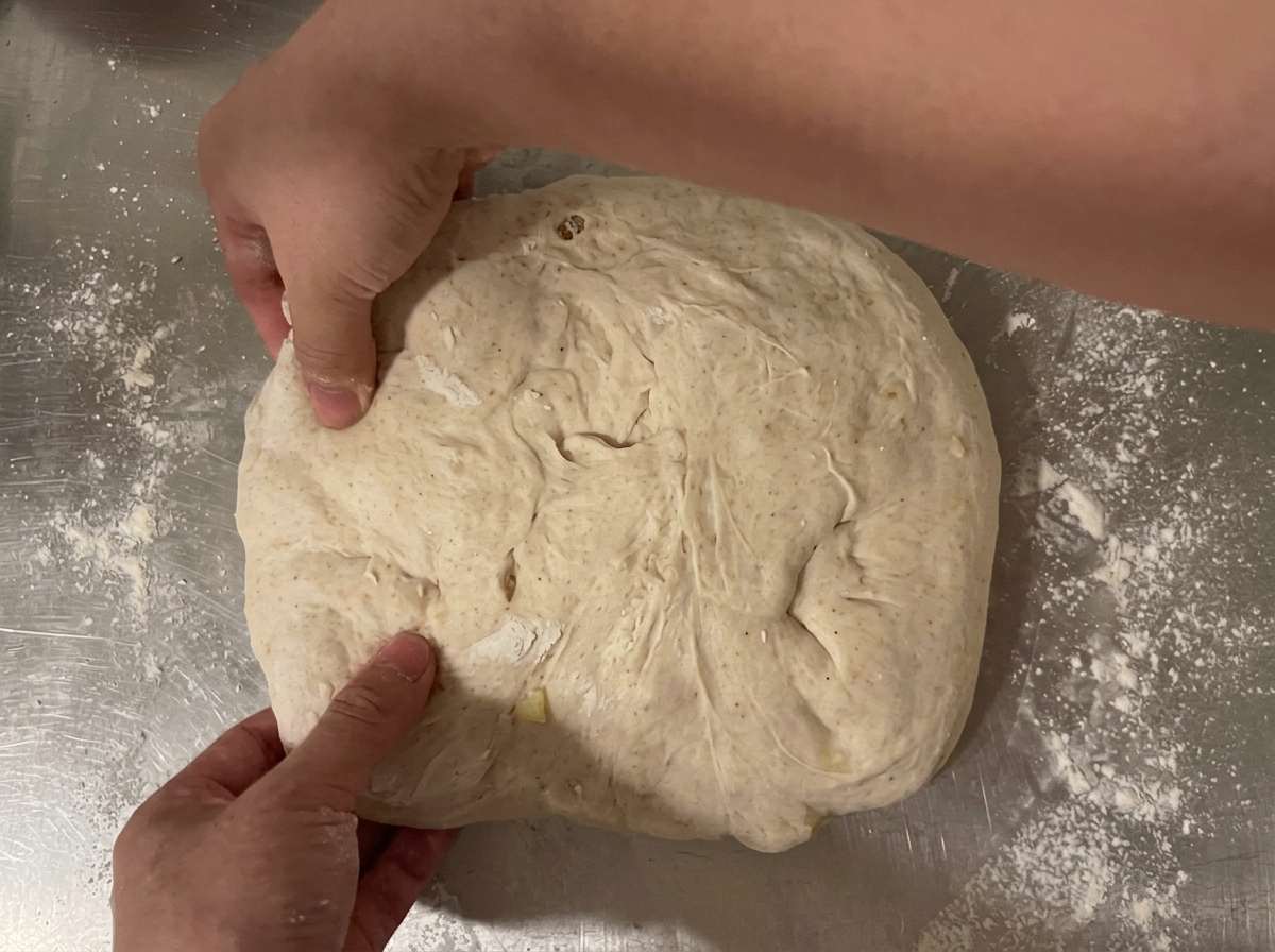 Dough being rolled into a loaf shape using the tri-fold method on a counter.