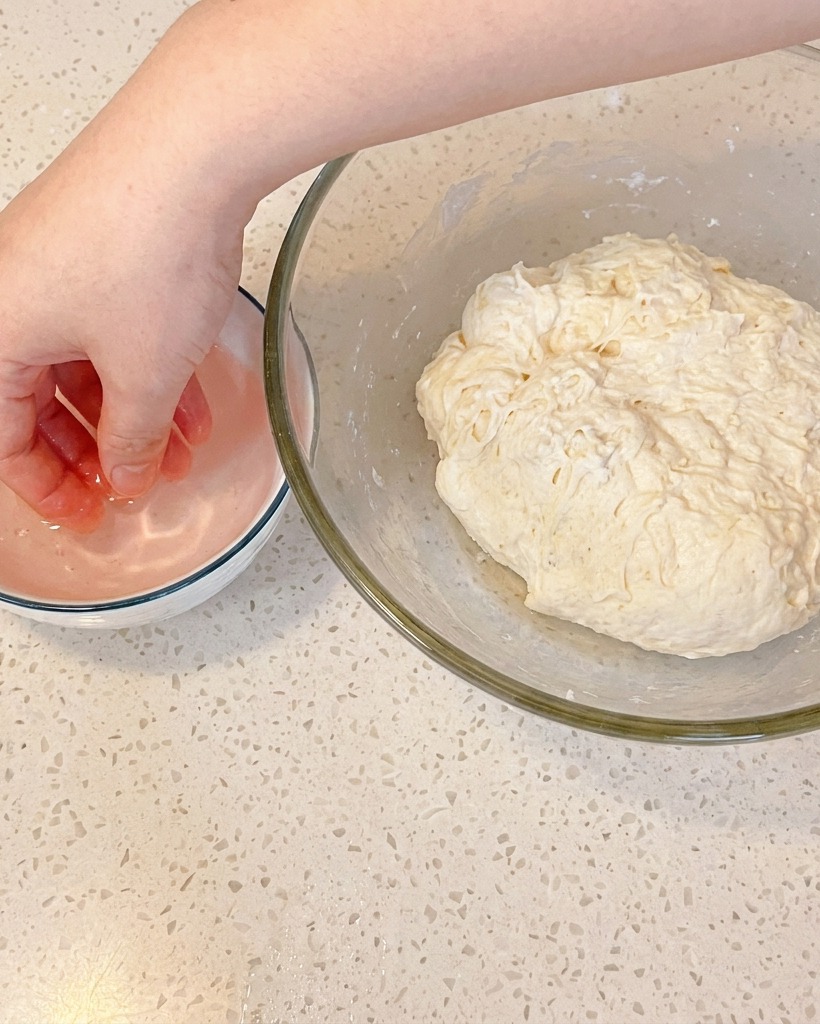 Close-up of a hand performing a fold on the dough in the bowl.