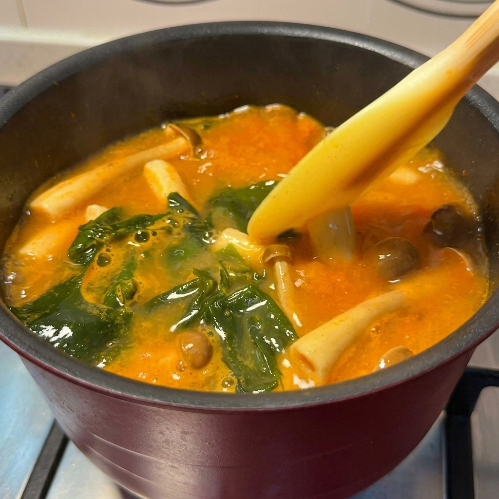 Golden-brown salmon chunks being added into a pot of simmering spicy miso soup.