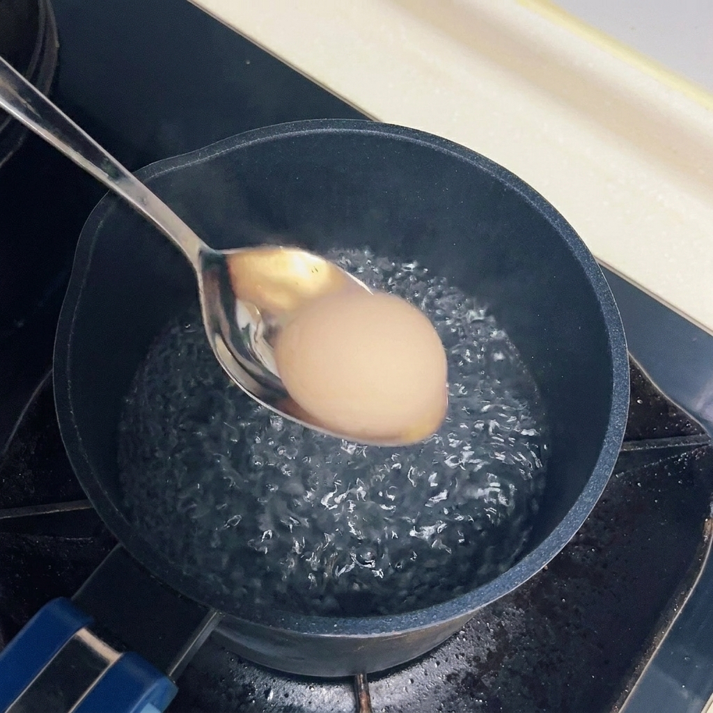 A single egg being carefully lowered into a pot of gently bubbling boiling water with a metal spoon.