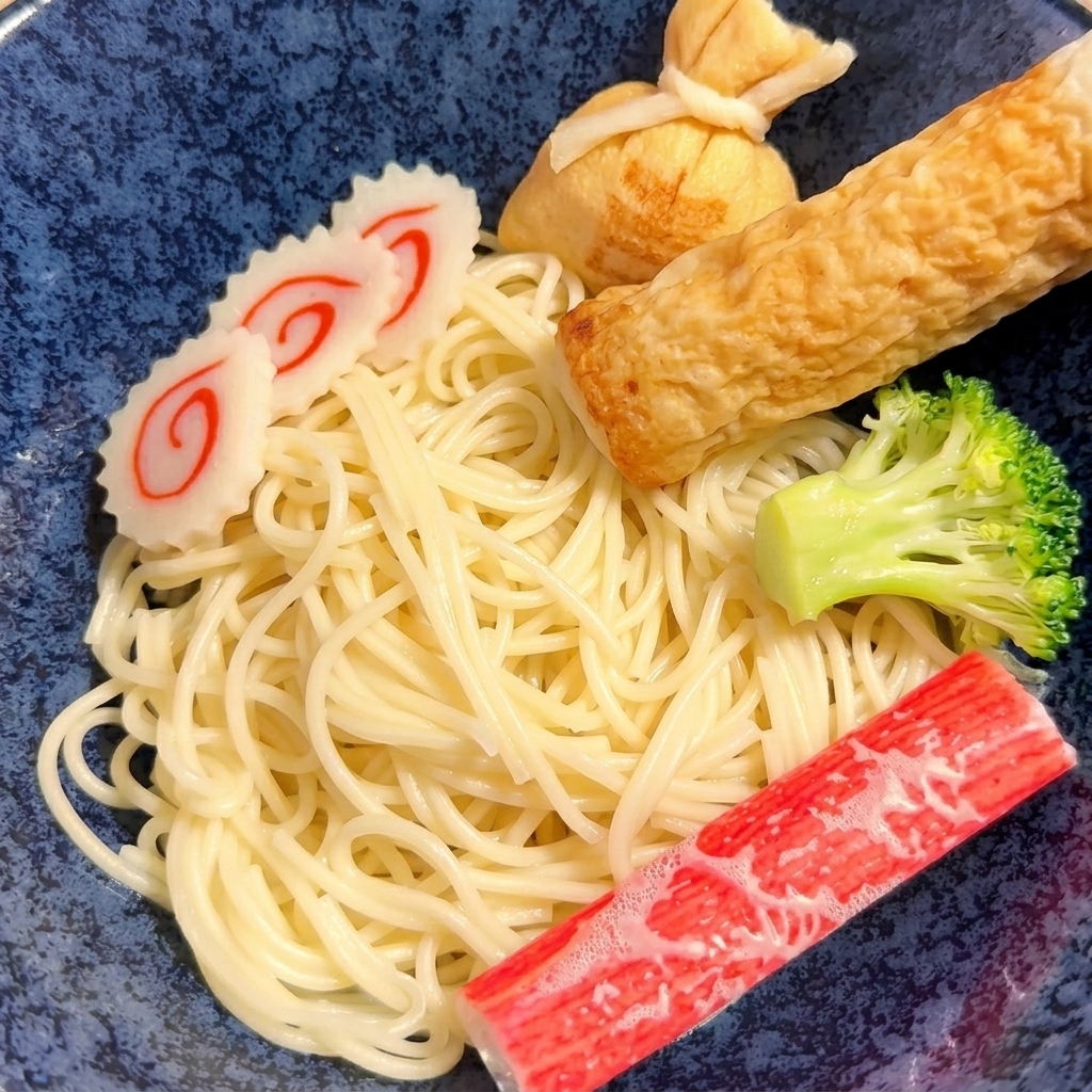 A pair of tongs placing cooked yellow noodles into a ceramic bowl.