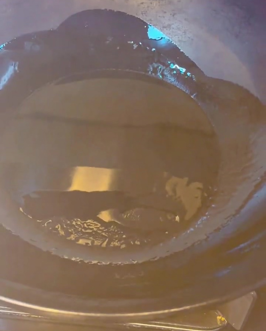Golden brown pork belly pieces frying in a hot wok with oil.