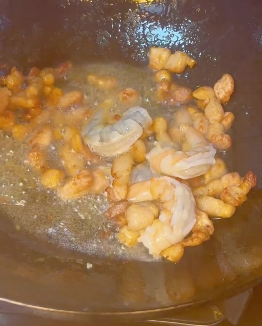 Shrimp, pork belly, and other mixed seafood stir-frying together in a hot wok.