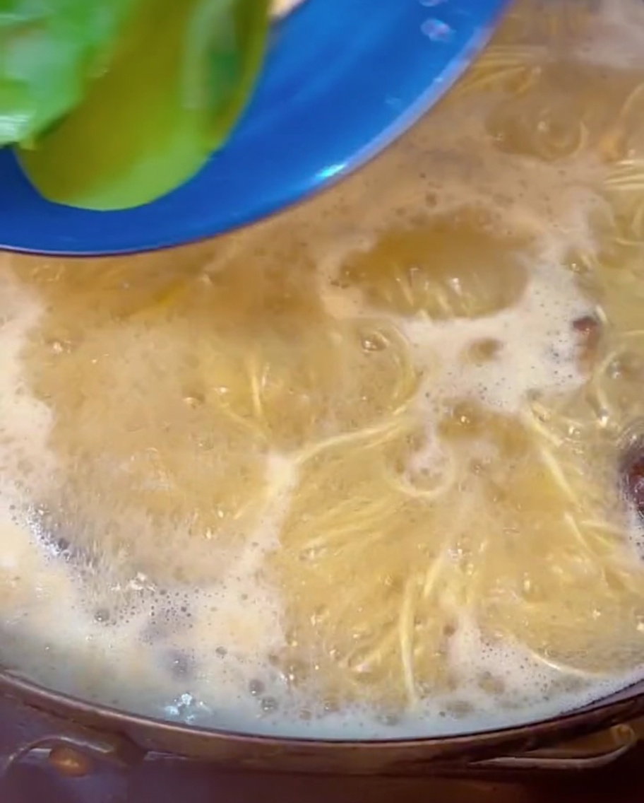 Fresh green bok choy being submerged into a pot of bubbling ramen noodles and broth.