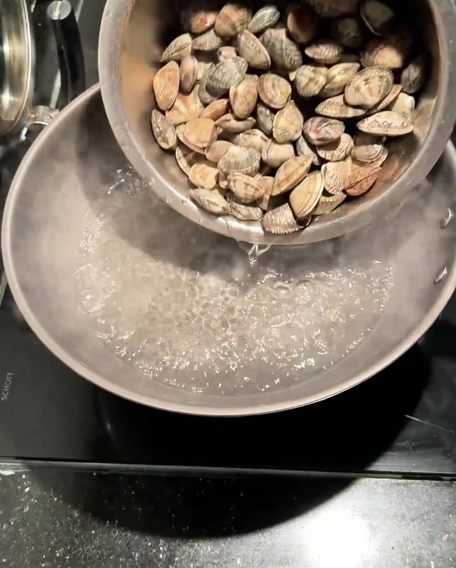 Fresh clams being poured into a pot of boiling salted water.