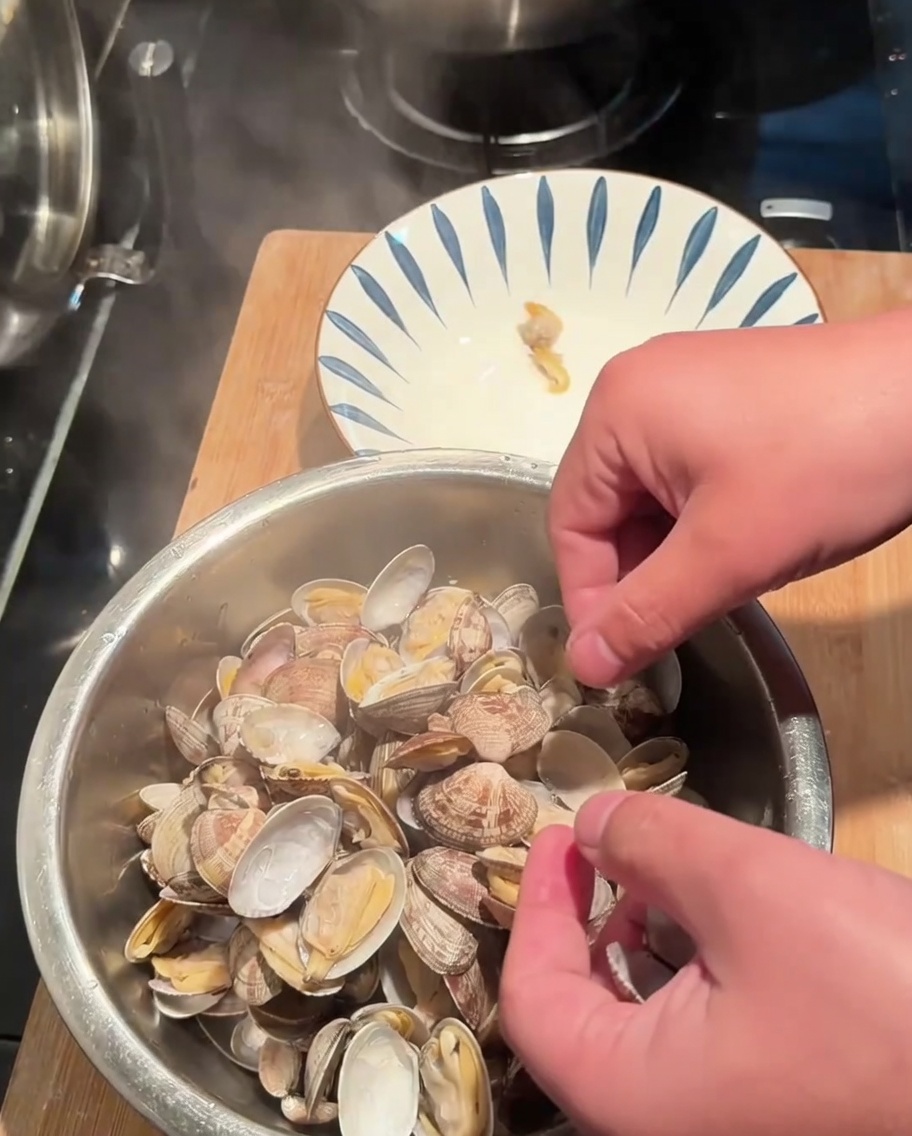 Hands removing clam meat from cooked shells into a bowl.