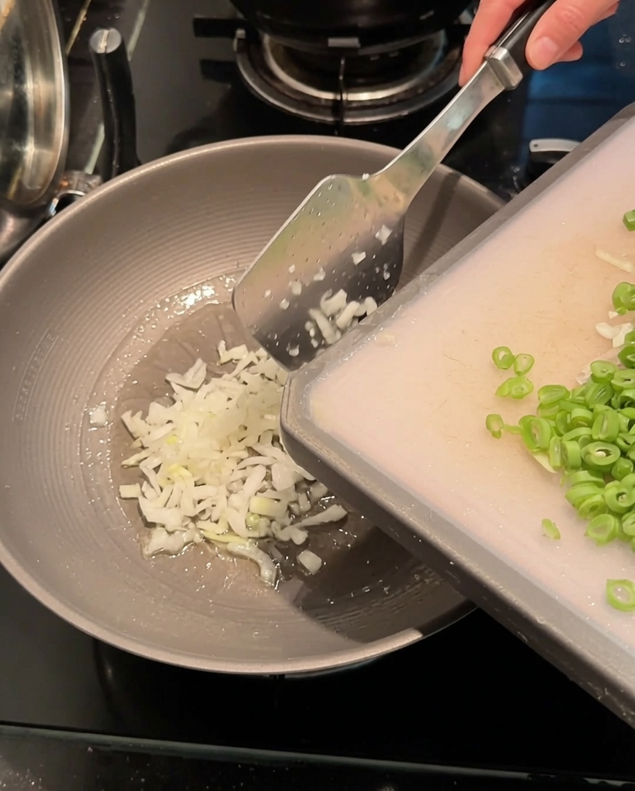 Minced green onions and sliced long beans being stir-fried in a hot wok with oil.