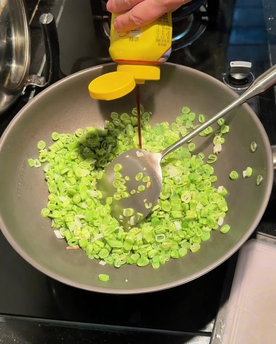 Squeezing seasoning sauce into a wok containing stir-frying beans and green onions.