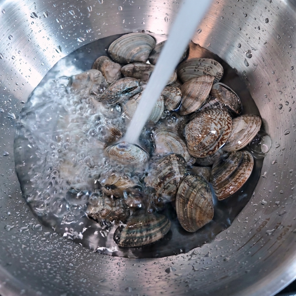 Running water pouring over fresh clams in a stainless steel bowl.