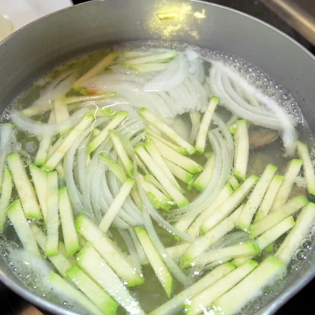 Close-up of seasonings like soy sauce and fish sauce being added to a pot of boiling vegetable broth.