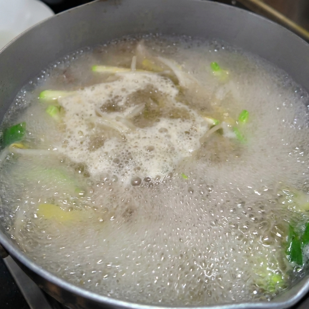 Fresh hand-pulled noodles being added to a pot of simmering vegetable and clam broth.