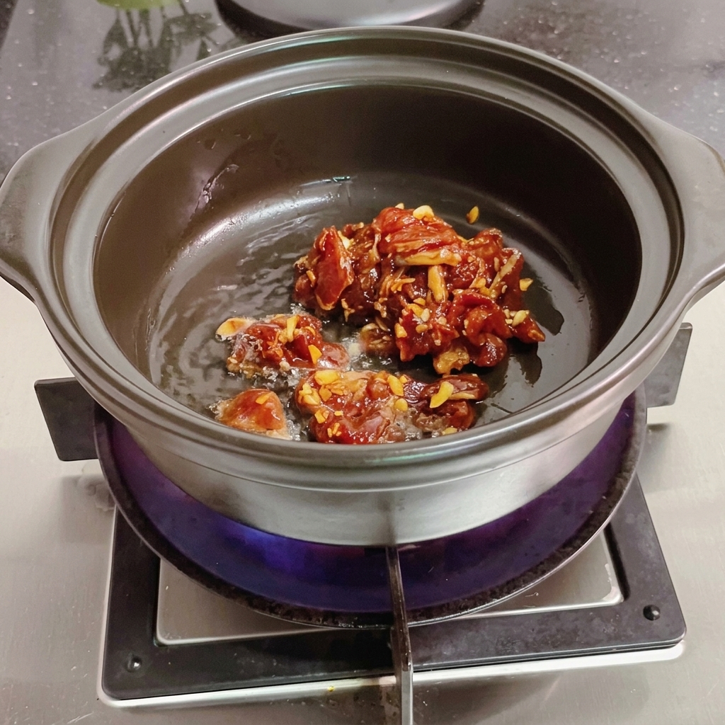 Meat slices being stirred in a clay pot with a wooden spatula.