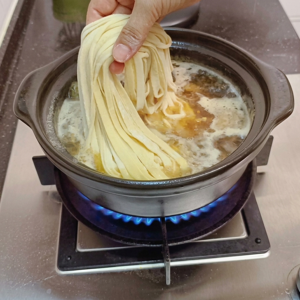 Handmade noodles being dropped into the simmering broth.
