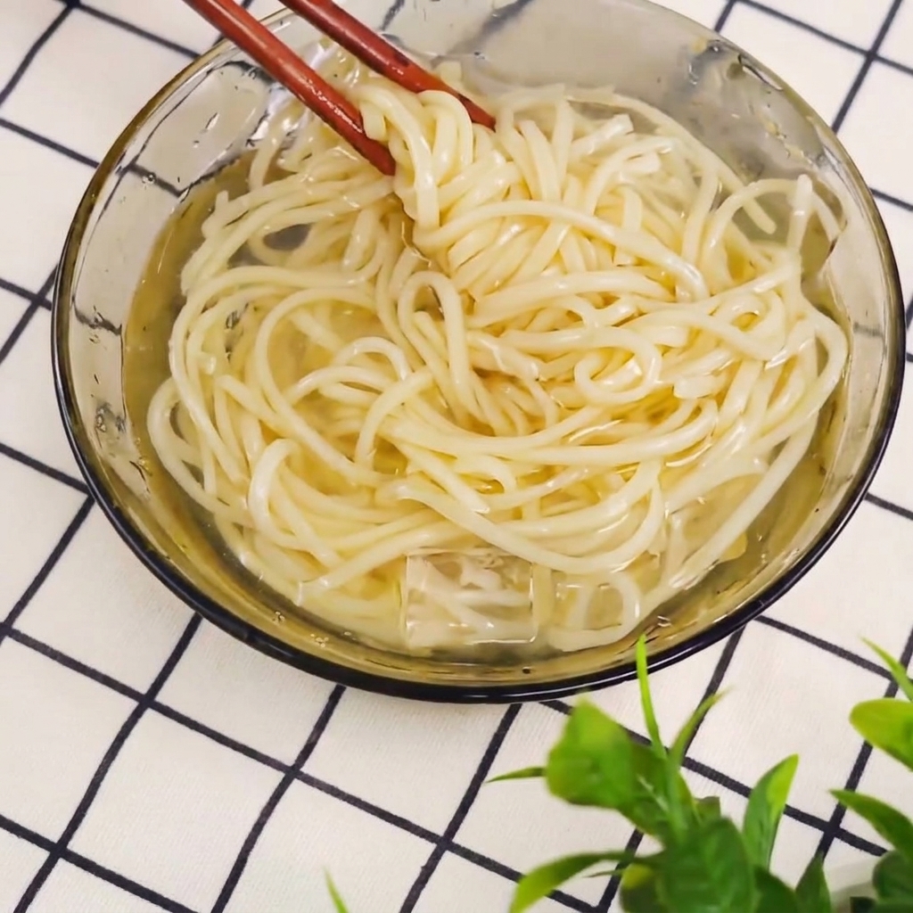 Cooked noodles being lifted out of a pot with chopsticks.