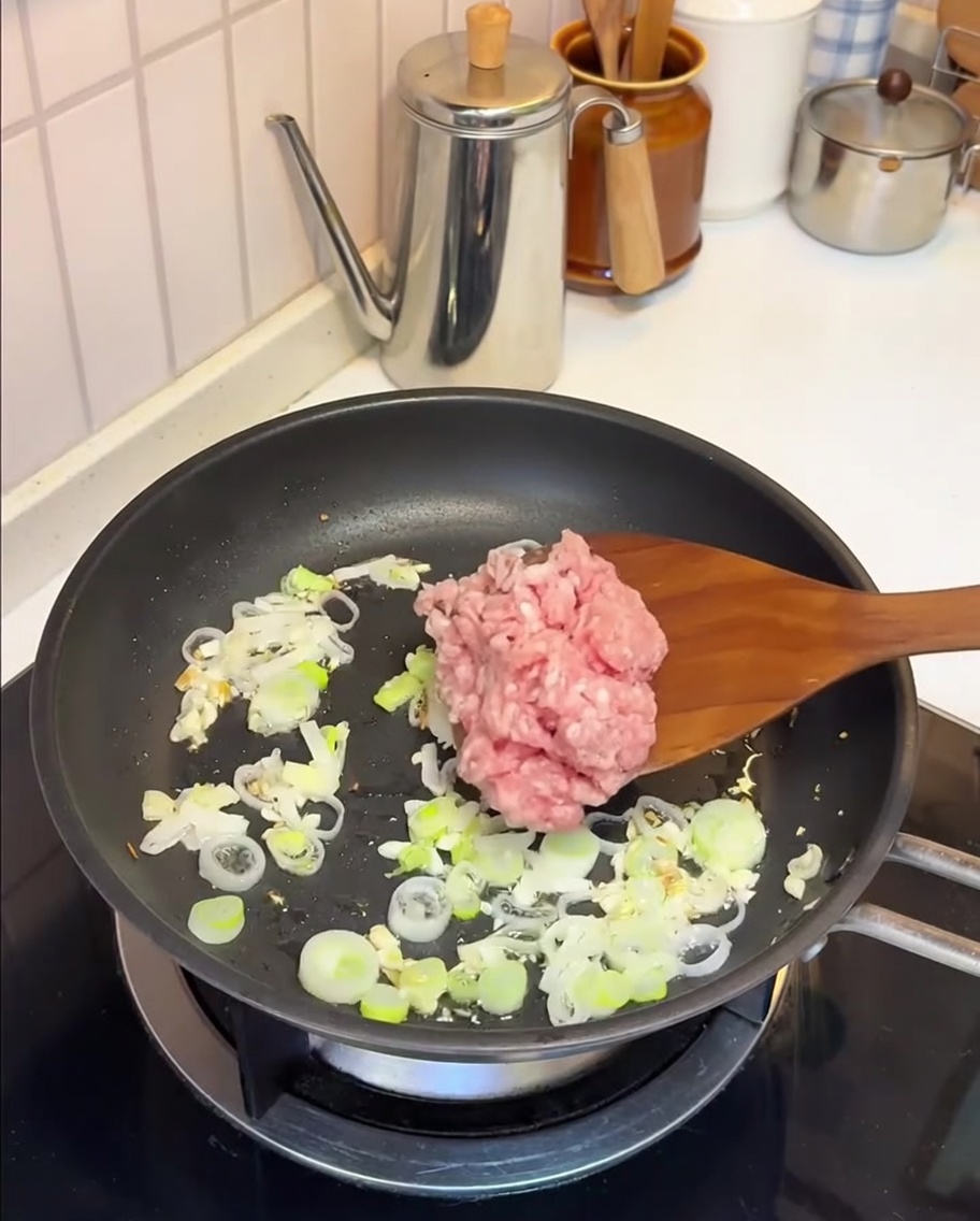 Ground pork being stir-fried in a pan with garlic and green onions.