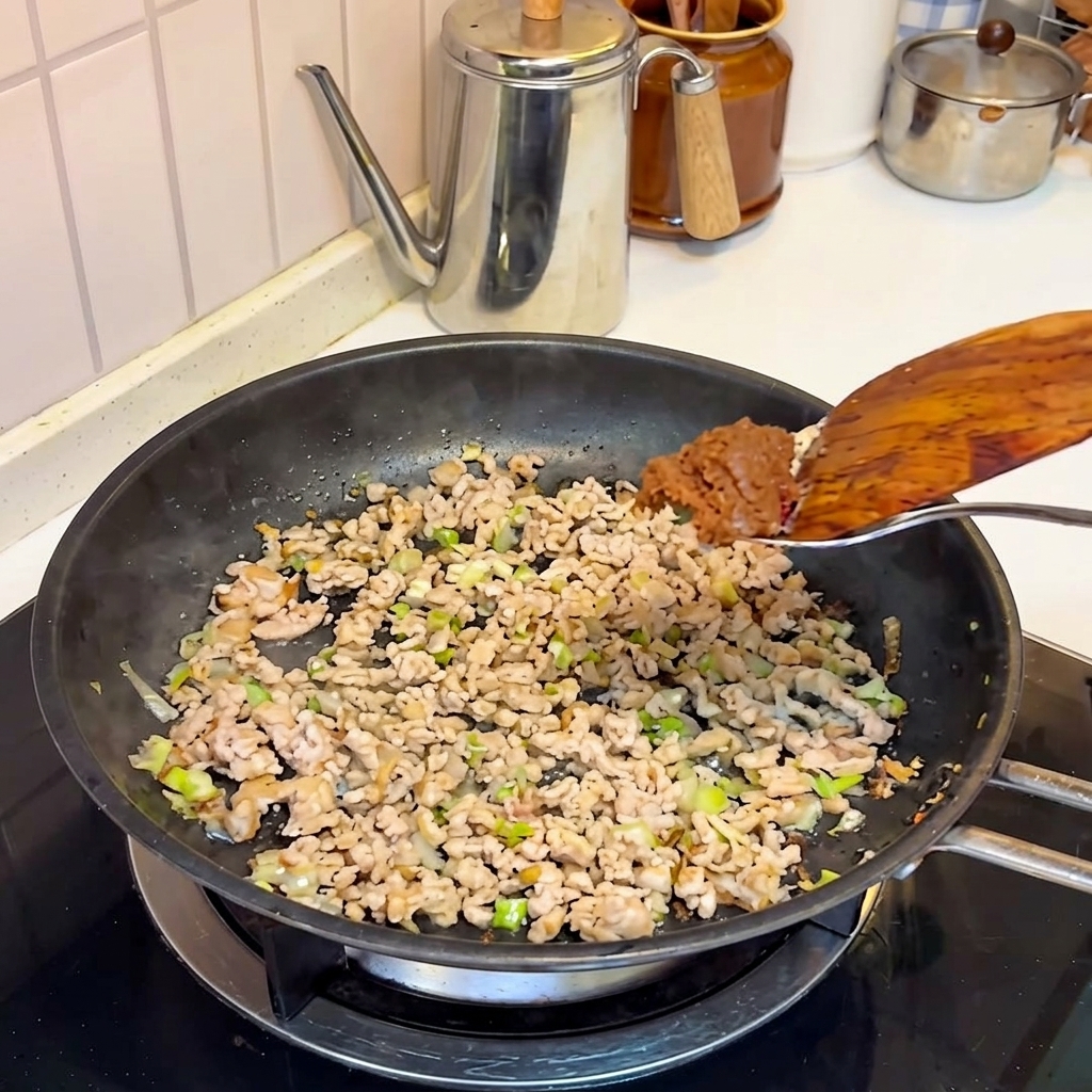 Miso paste being added to the cooked pork in the frying pan.