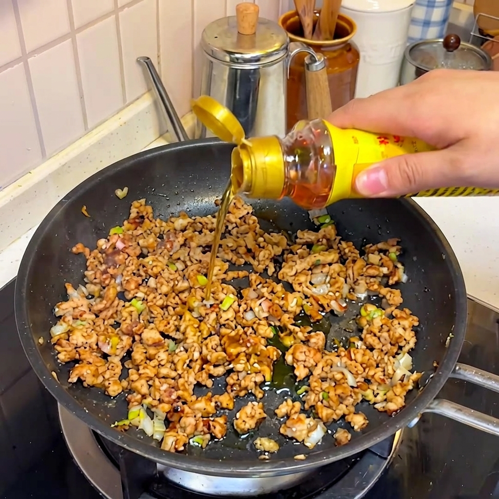 Sesame oil and other seasonings being poured onto the seasoned pork mixture.