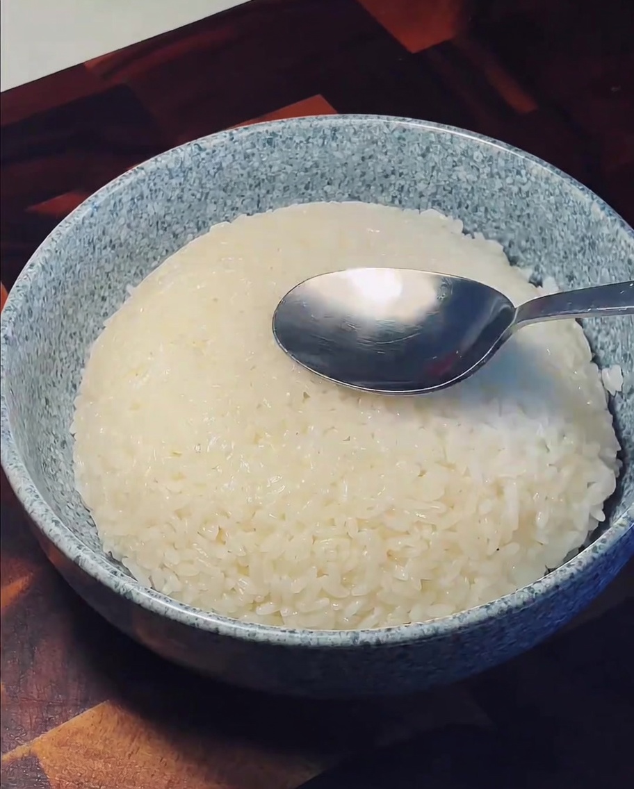 A metal spoon pressing down into the center of a mound of fluffy white rice in a ceramic bowl.