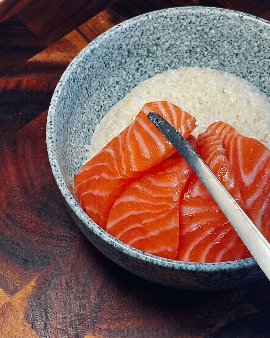 Fresh, bright orange salmon slices being arranged in an overlapping circle on top of white rice.
