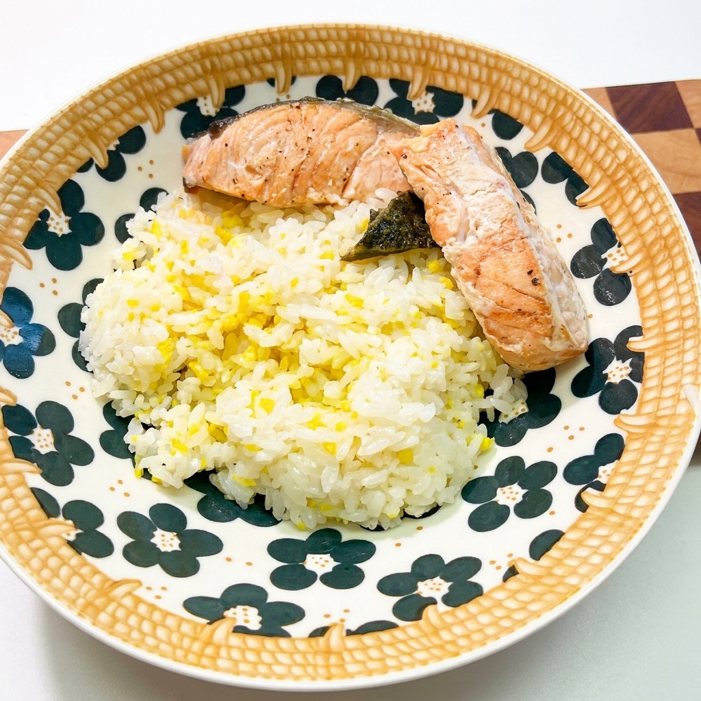 A beautifully patterned ceramic bowl filled with white rice, topped with two pieces of cooked salmon and dark seaweed.